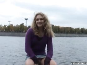 Миленькая девушка в короткой юбке расставляет ноги на набережной